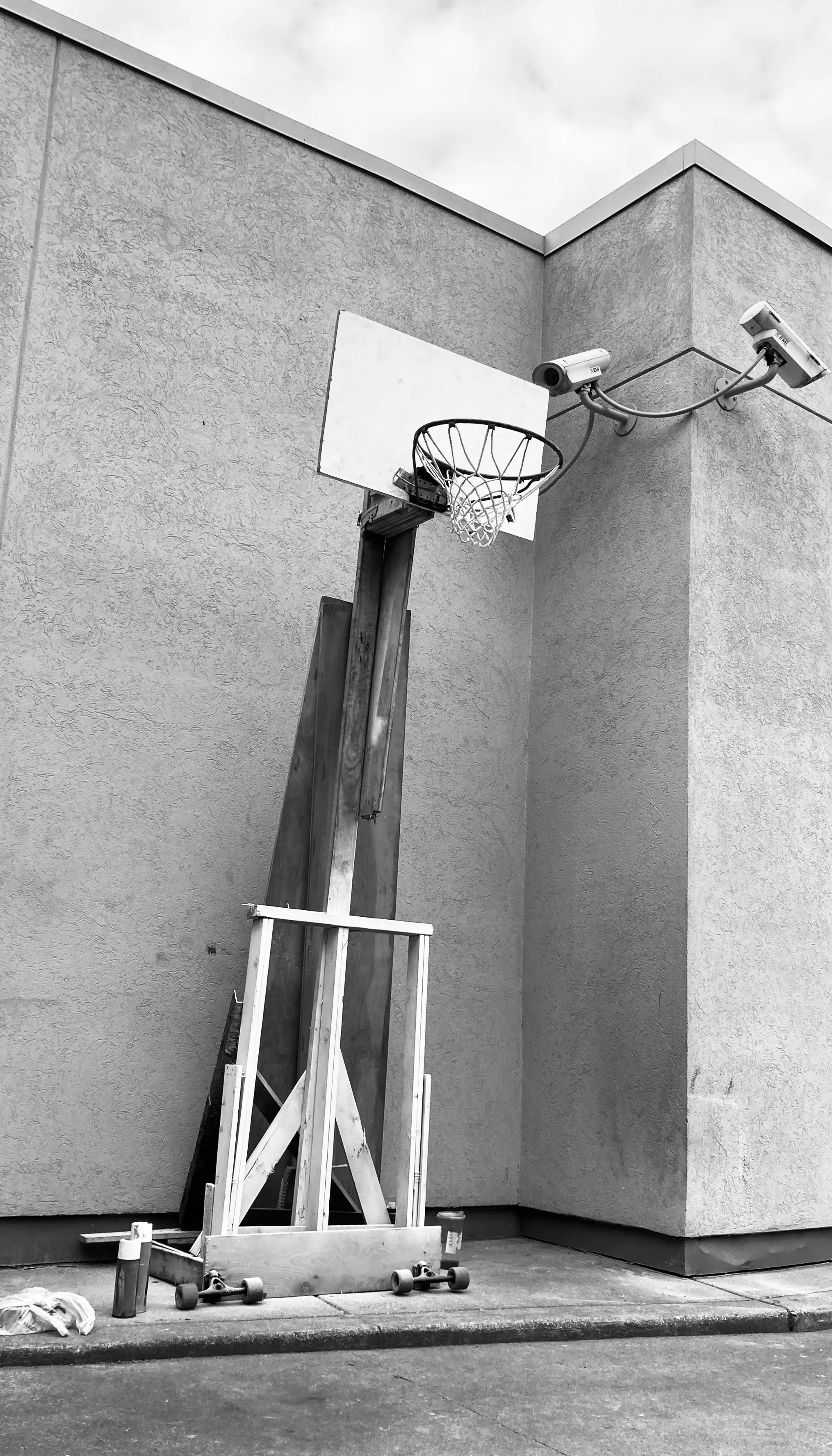 Homemade wooden basketball hoop propped against a building under security cameras